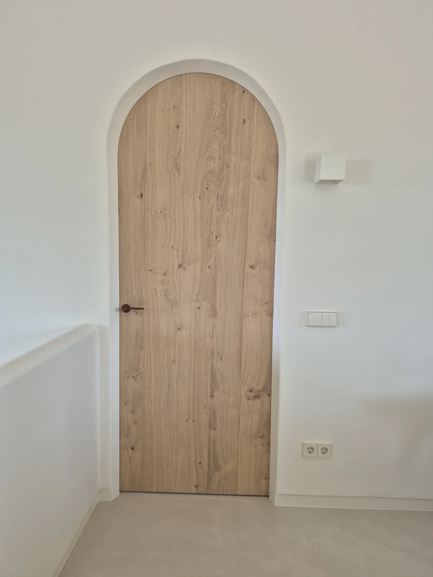Puerta de roble macizo recortada en arco sobre paramento blanco — Casa Bancal