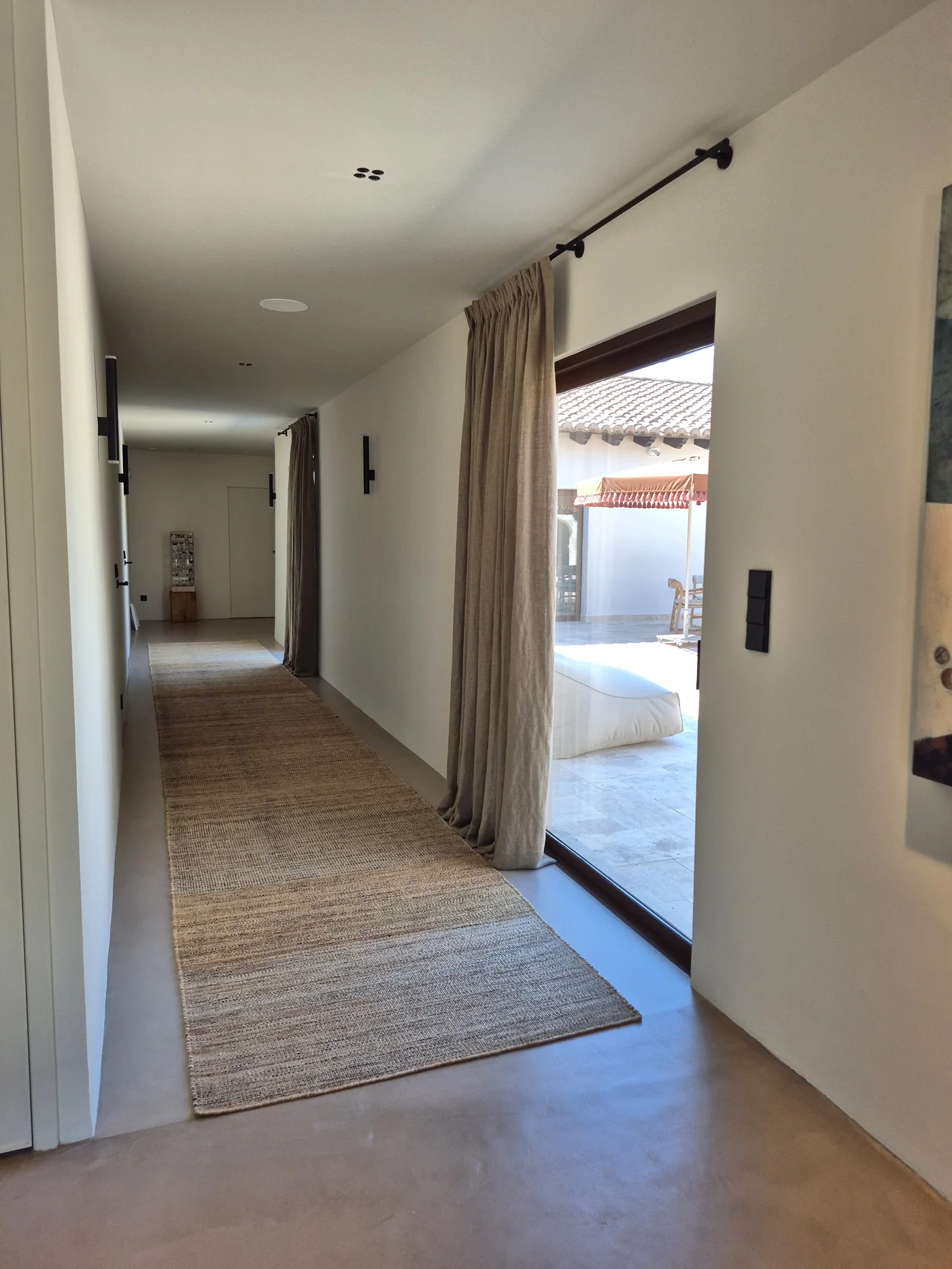 Pasillo con alfombra de yute a medida y cortinas de lino de suelo a techo sobre microcemento continuo — La Cumbre, Benissa